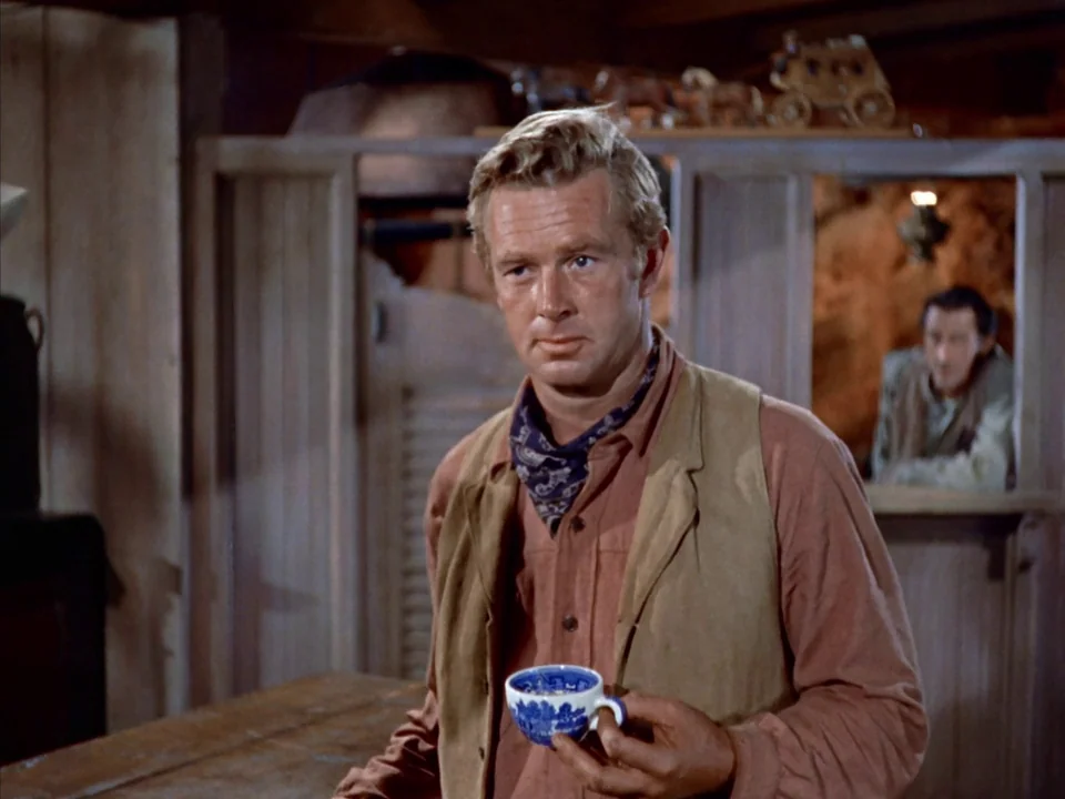 Johnny Guitar (1954) movie still: medium — A wooden saloon interior with a partial wall divider and a bar counter. A man stands at the counter…