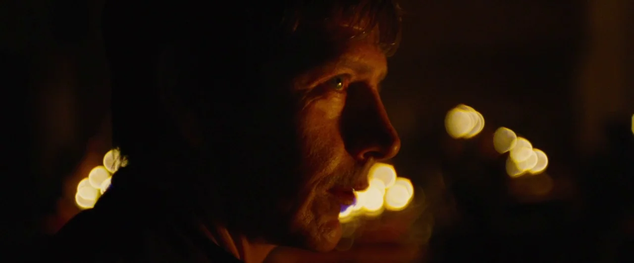 Lost River (2014) movie still: closeup — A dark, dimly lit interior space contains a man looking toward the right. Out-of-focus golden light circles…