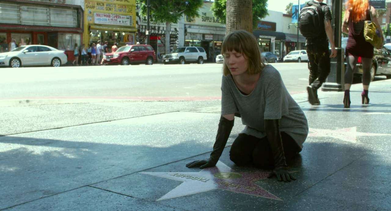 Maps to the Stars (2014) movie still: fullbody — An urban sidewalk displays embedded star markers against a backdrop of storefronts and cars. A…