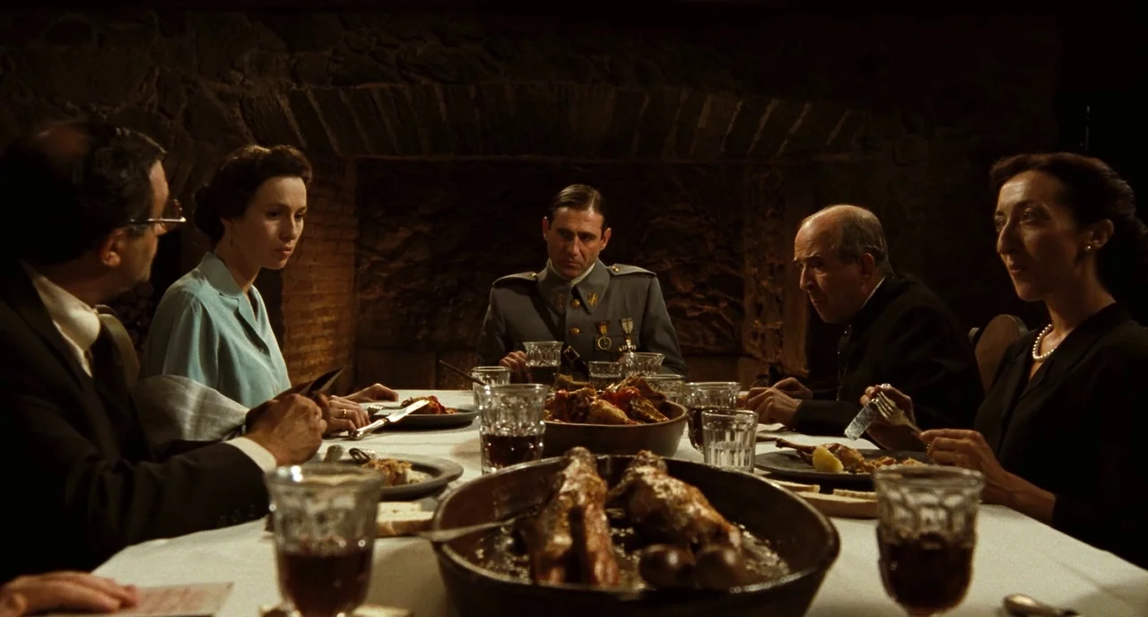 Pan’s Labyrinth (2006) movie still: medium — A stone-walled dining hall is set with a long, white-clothed table for a feast. Five individuals in…