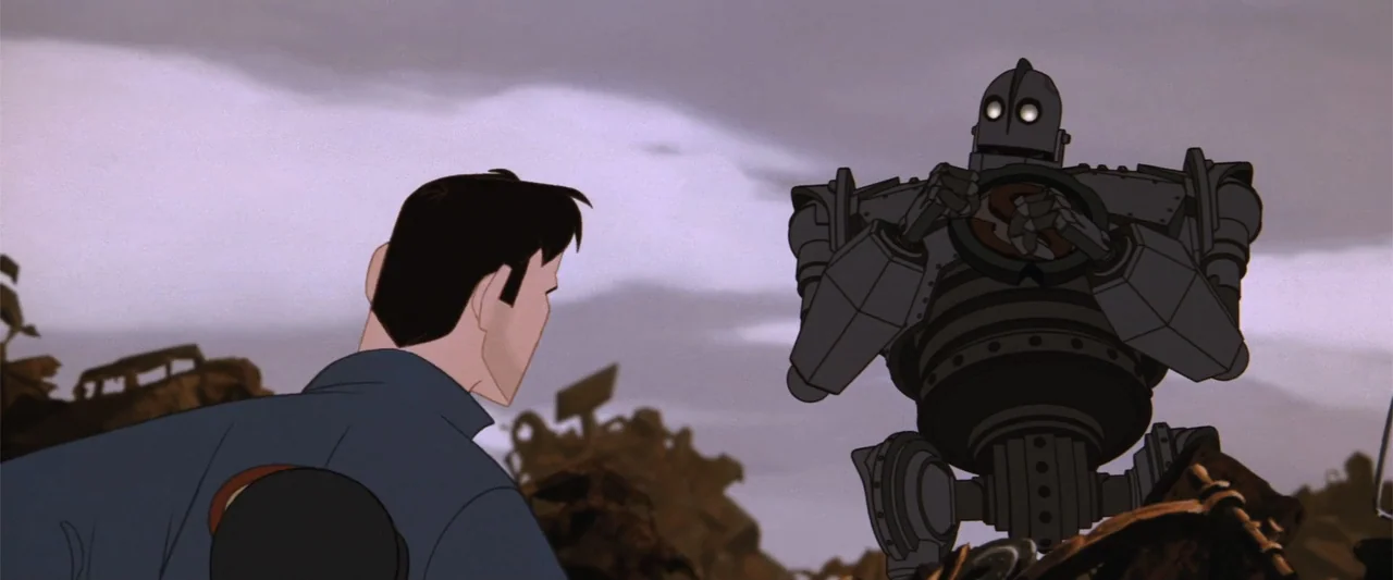 The Iron Giant (1999) movie still: medium — A sprawling outdoor scrap yard filled with piles of rusted metal and debris. A human male stands facing…