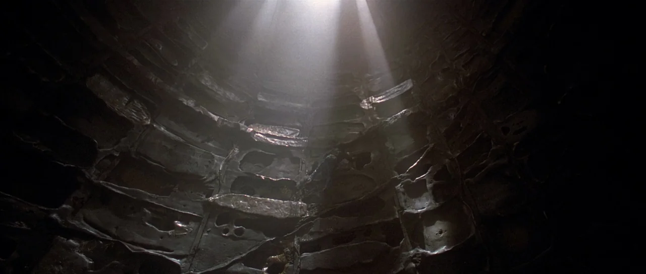 Fire In The Sky (1993) movie still: wide — A dark, cavernous space is constructed from dark, organic-looking panels with irregular, textured…