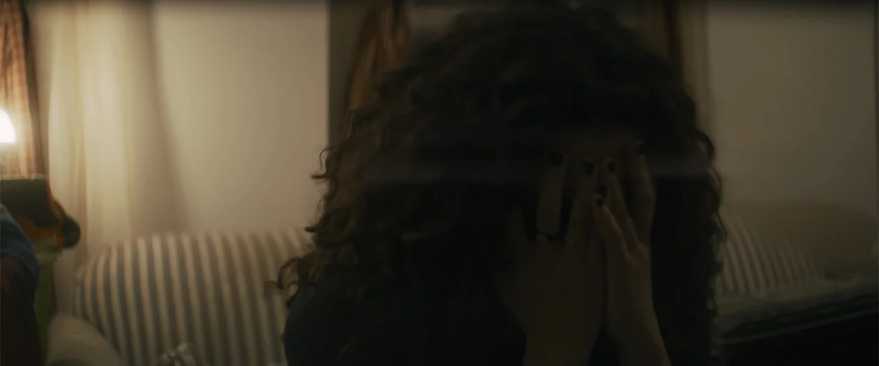 Holiday Harmony (2022) movie still: closeup — A dimly lit indoor space features a striped sofa in the background. A woman with voluminous dark curly…