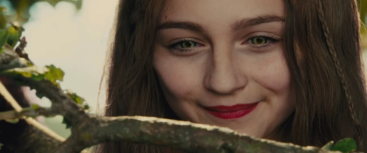 Maleficent (2014) movie still: closeup — A person looks through branches in an outdoor setting filled with dappled sunlight. She gazes directly into…