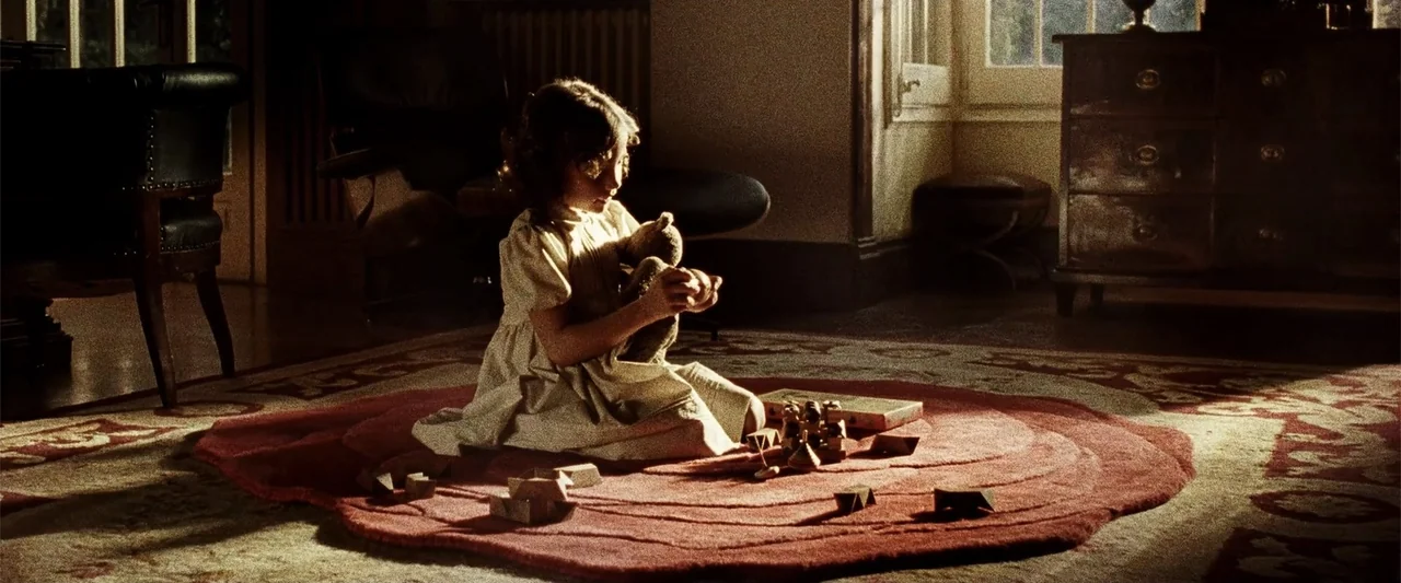Anna (2013) movie still: medium — A dimly lit room with vintage furniture and a large red circular rug. A young girl sits on the floor playing with…
