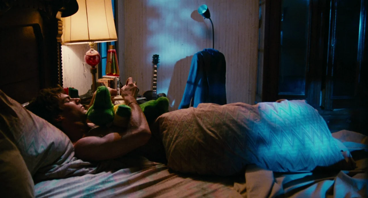 The Big Easy (1986) movie still: medium — A bedroom at night contains a unmade bed and personal clutter. A young man lies on the pillows while…