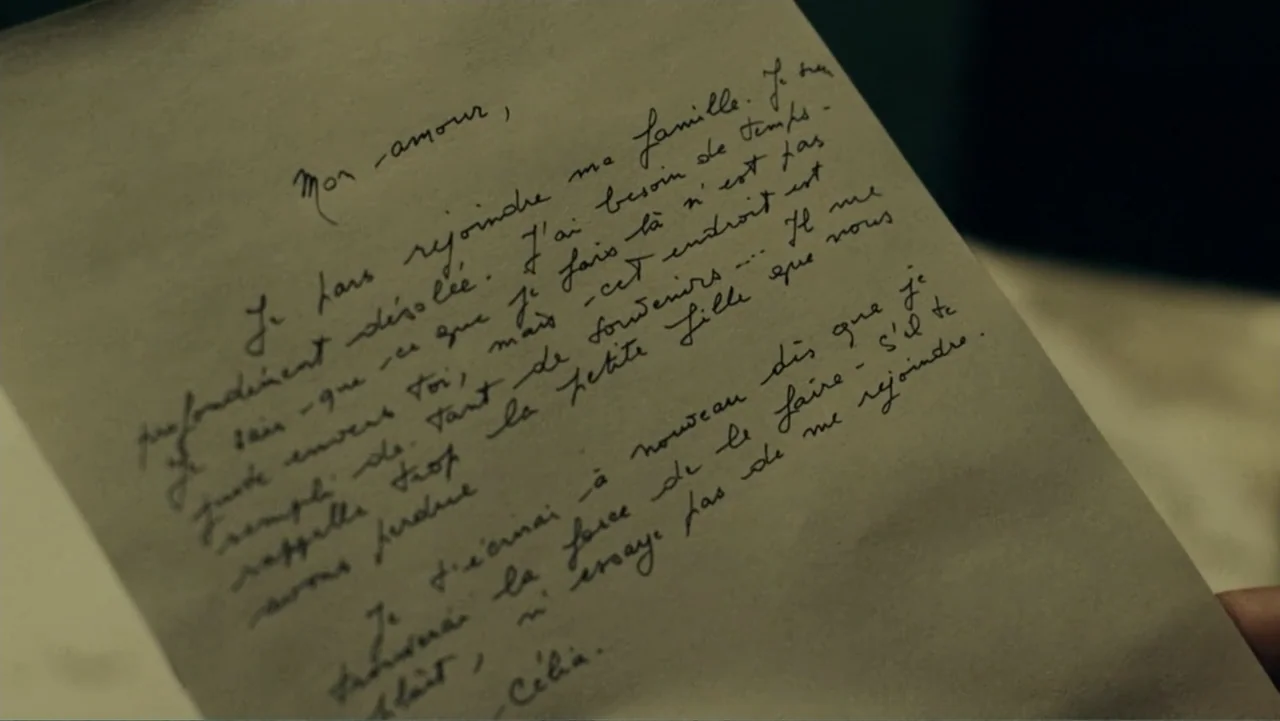 The Words (2012) movie still: closeup — A piece of aged paper with cursive French handwriting sits in bright light. The paper has a rough texture…