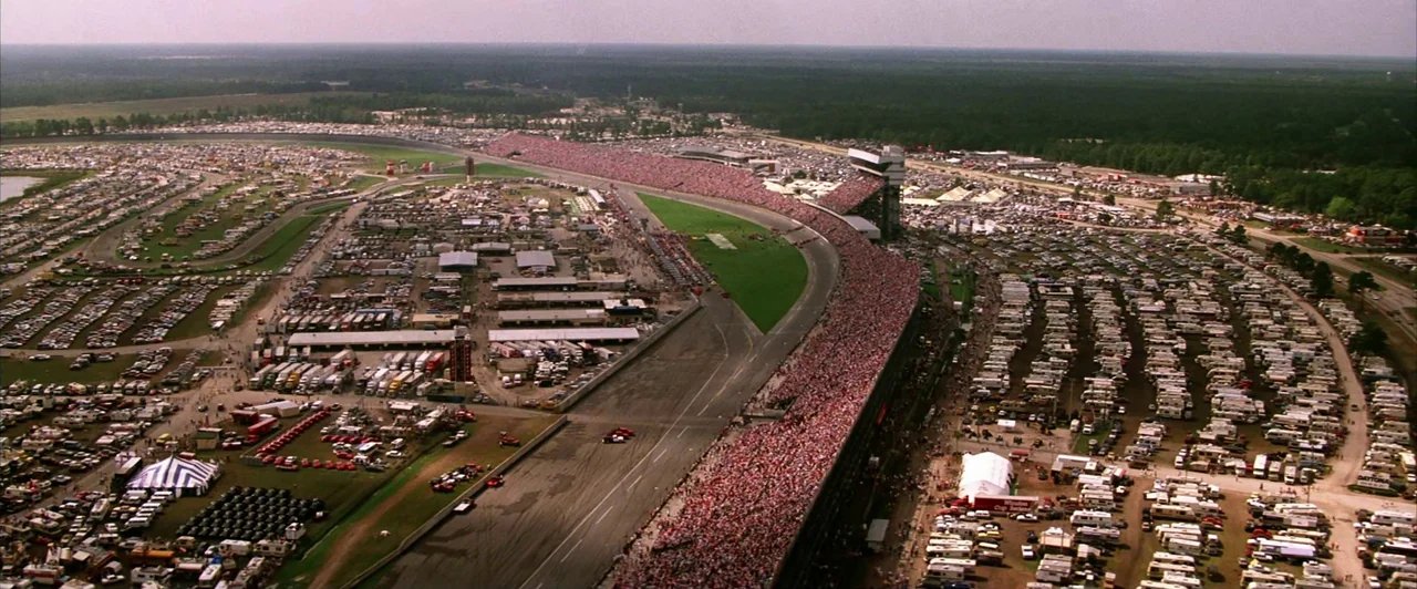 Days of Thunder (1990) movie still: establishing — A vast aerial view shows the Daytona International Speedway packed with fans and campers.…