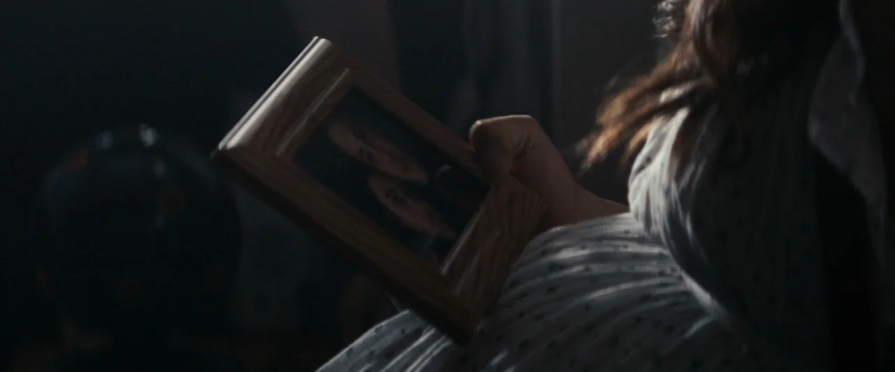 Strange but True (2019) movie still: closeup — A dimly lit interior room with blurred surroundings and shadow-obscured features. A person's hand…