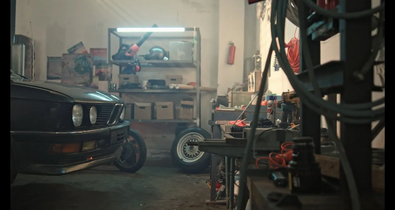 Hunted by My Husband: The Untold Story of the DC Sniper (2025) movie still: medium — A cluttered auto repair garage contains car parts and tools on…