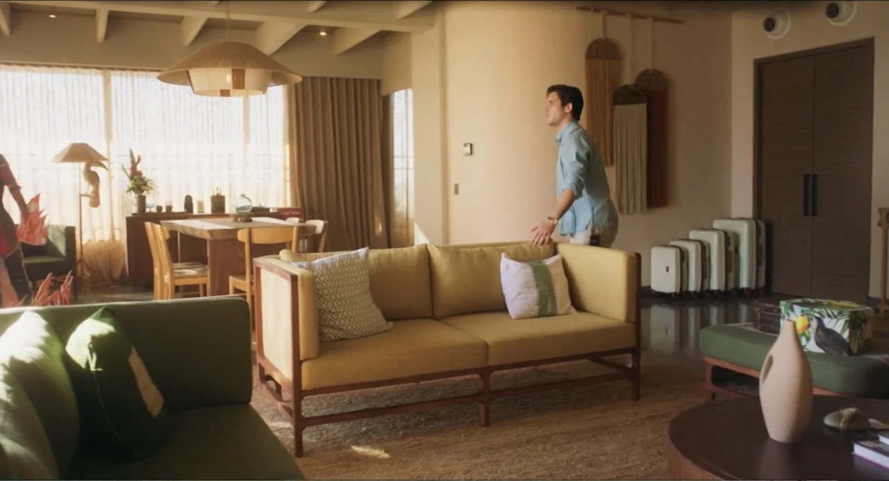 At Midnight (2023) movie still: medium — A contemporary living room features wood furniture, beige walls, and various decorative wall hangings. A…