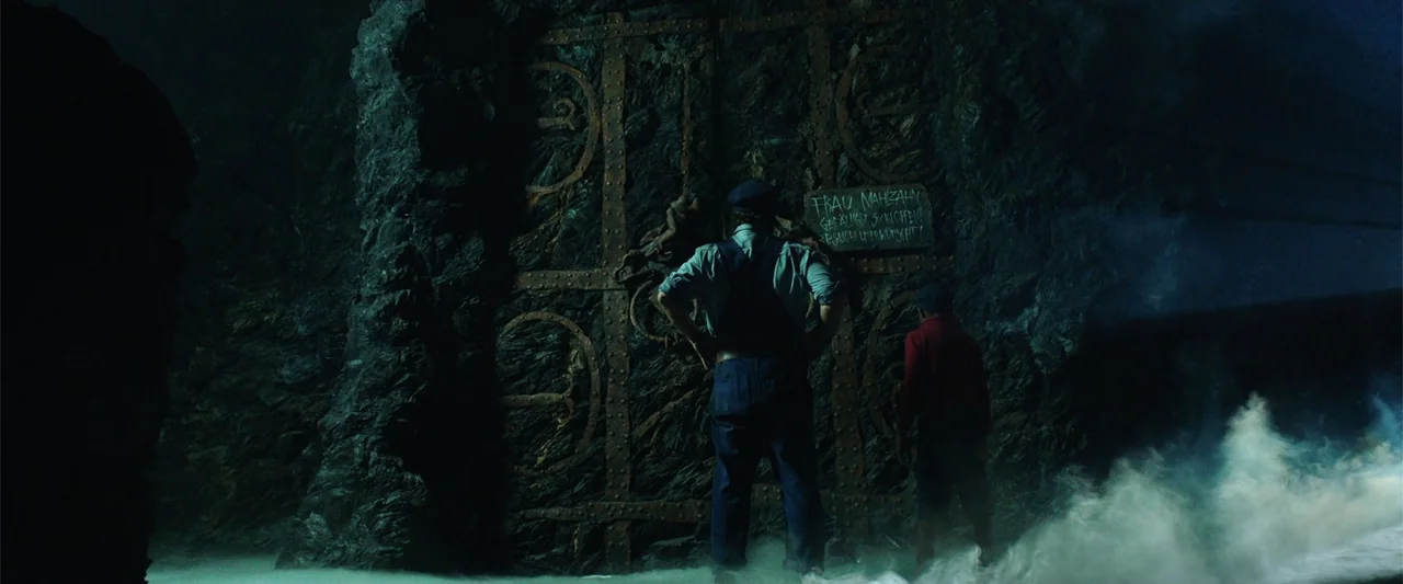 Jim Button and Luke the Engine Driver (2018) movie still: fullbody — Two individuals stand before a massive ornate metal door embedded in a jagged…