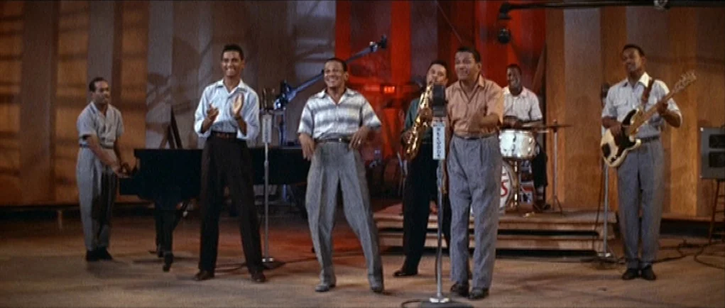 The Girl Can’t Help It (1956) movie still: fullbody — A spacious wood-paneled room functions as a music recording studio with instruments arranged…
