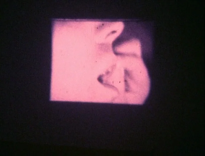 Glitterbug (1994) movie still: closeup — A rectangular frame shows a close-up of a kiss projected against a dark background. The film exhibits grain…