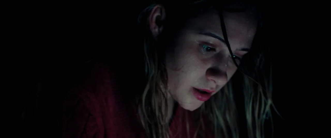 Bodies Bodies Bodies (2022) movie still: closeup — A person is in a dark, shadow-filled environment with no visible background details. The woman's…
