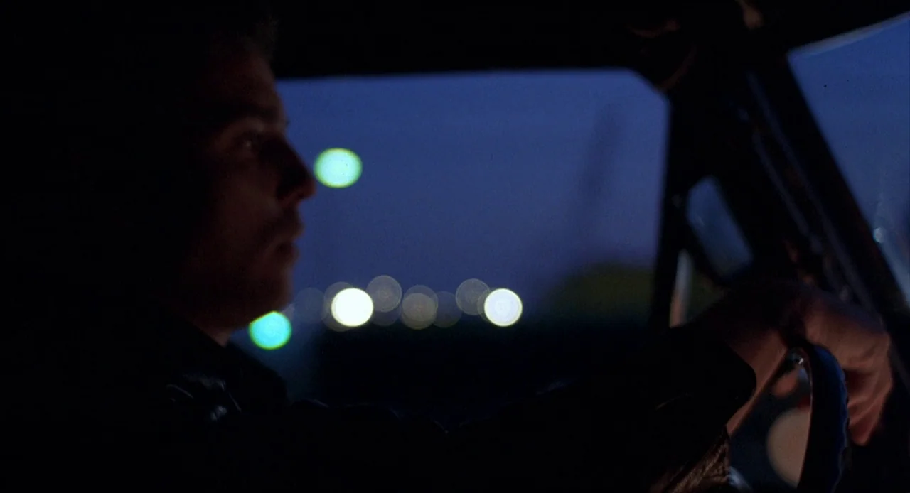 To Live and Die in L.A. (1985) movie still: medium — A dark vehicle interior with the driver partially visible in profile against a window. Blurred…