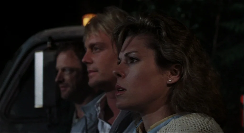 Evil Dead II (1987) movie still: medium — A dark night setting inside the cab of a parked pickup truck. Three individuals look forward through the…
