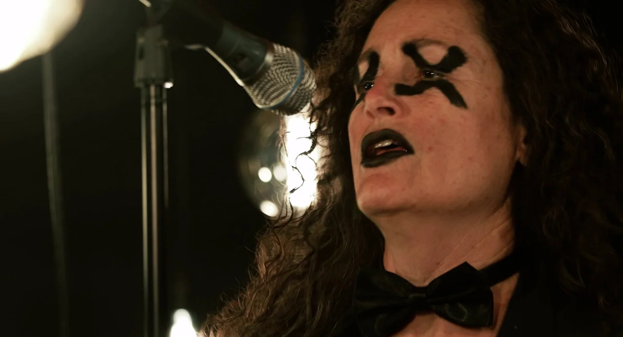 Hellbender (2021) movie still: closeup — A dark stage environment featuring a single performer under stark directional lighting. The subject…