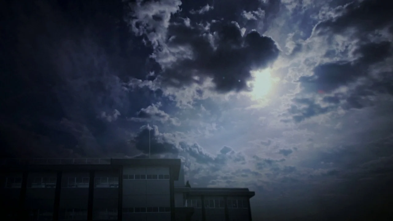 Confessions (2010) movie still: establishing — A dark, silhouetted school building sits against a cloudy night sky. The moon shines through the…