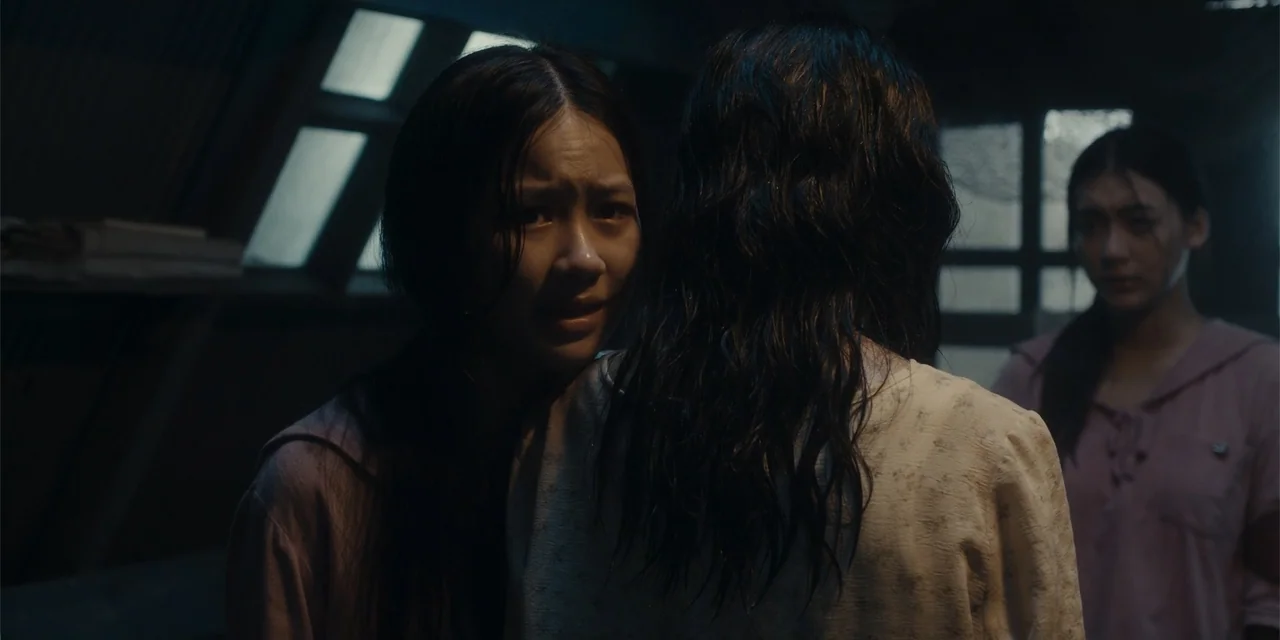 Host (2020) movie still: medium — A dimly lit room features a window with grid patterns in the background. Two young women stand near each other in…