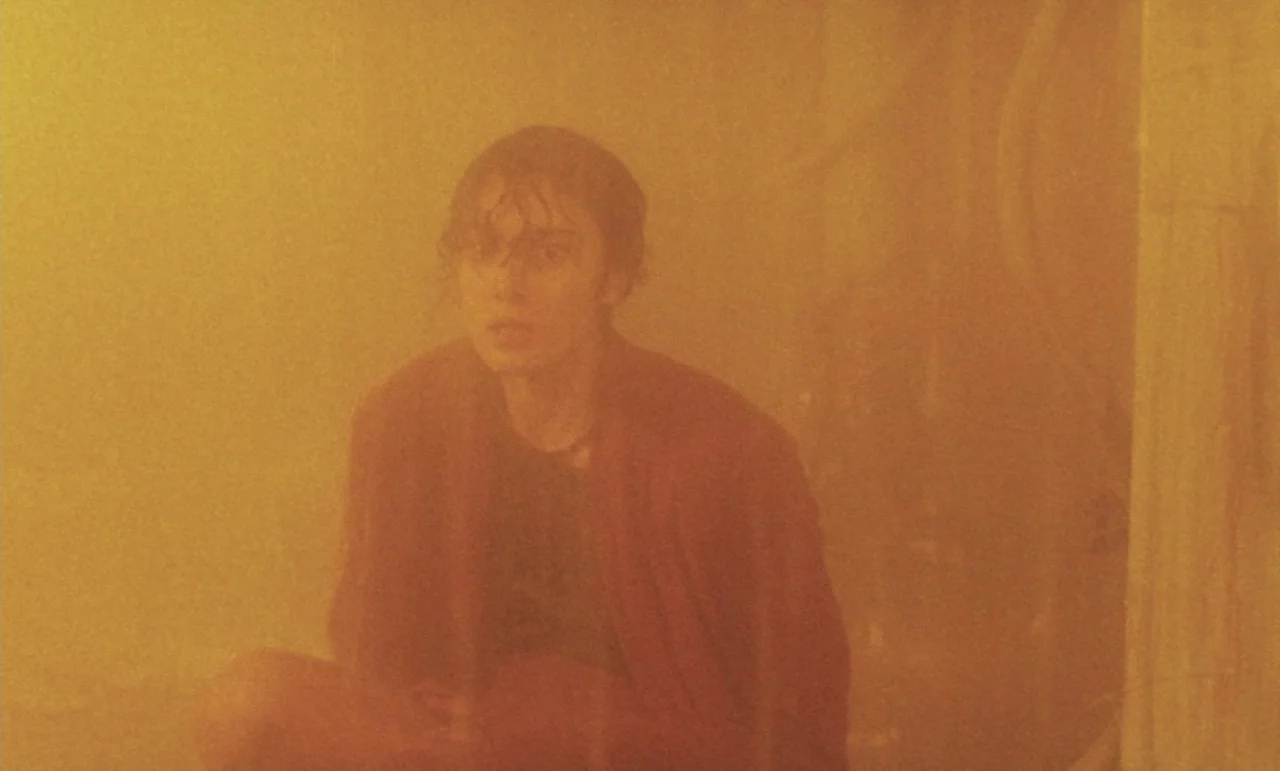 Evil Dead Trap (1988) movie still: medium — A person sits within a small interior space obscured by a thick amber haze. The subject stares ahead…