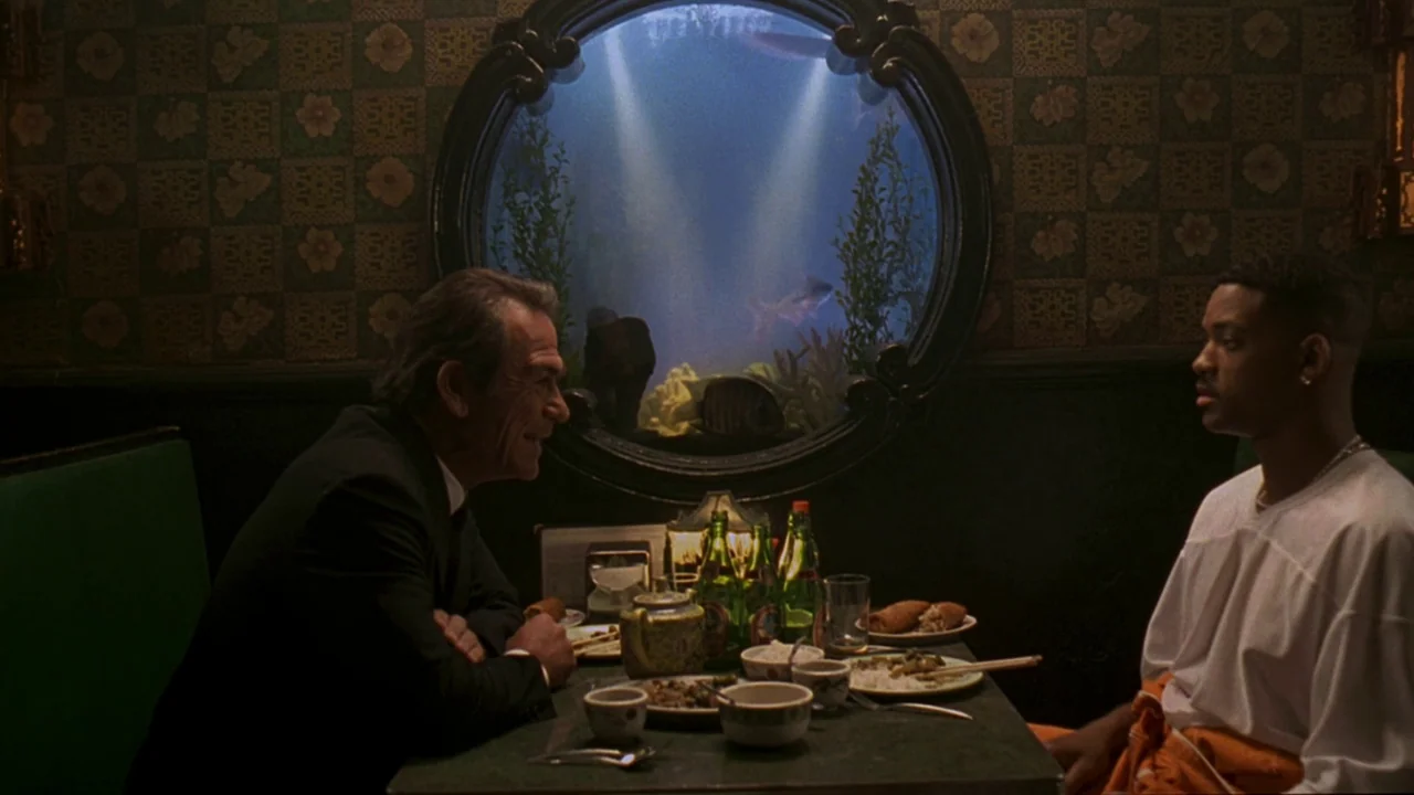 Men In Black (1997) movie still: medium — An intimate restaurant booth features a round aquarium mounted on the back wall. An older man in a suit…