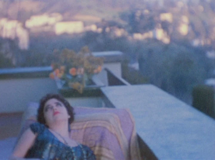 Puce Moment (1949) movie still: medium — A stone balcony terrace overlooks a soft-focused hilly landscape during dusk. A woman lies on a lounge…
