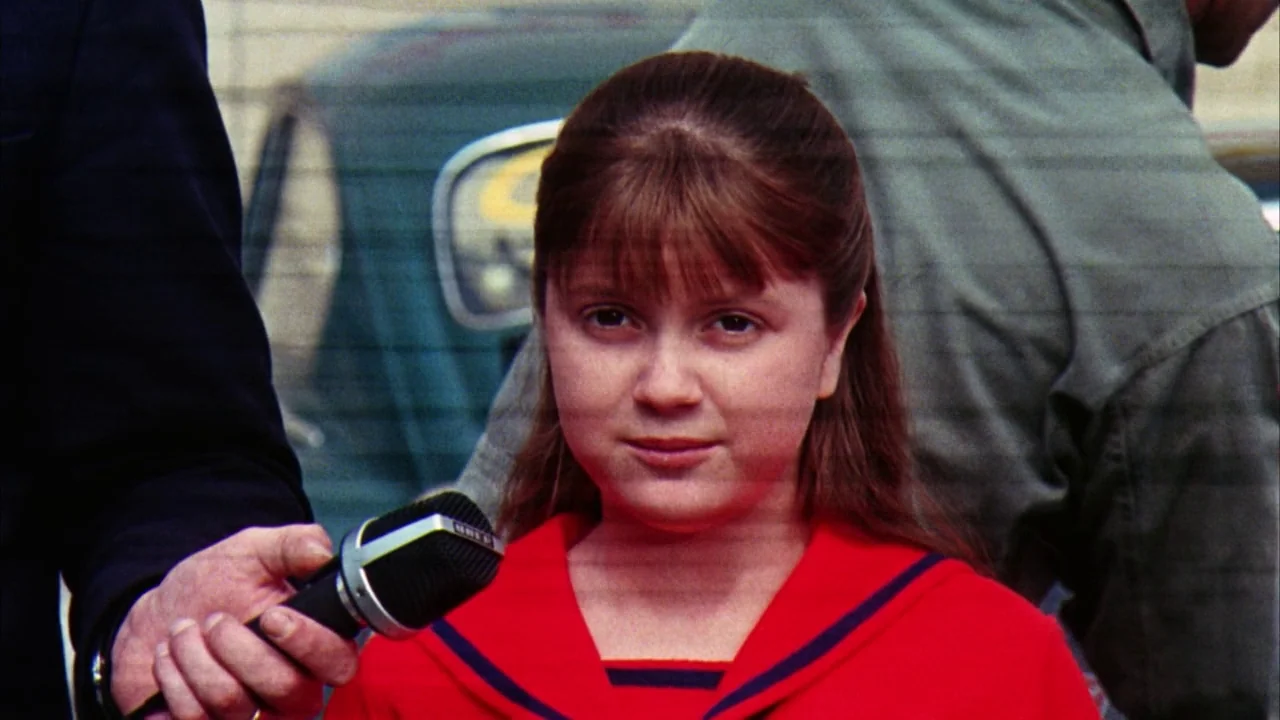 Willy Wonka & the Chocolate Factory (1971) movie still: closeup — A young girl stands in an outdoor urban setting during the day. She holds a…