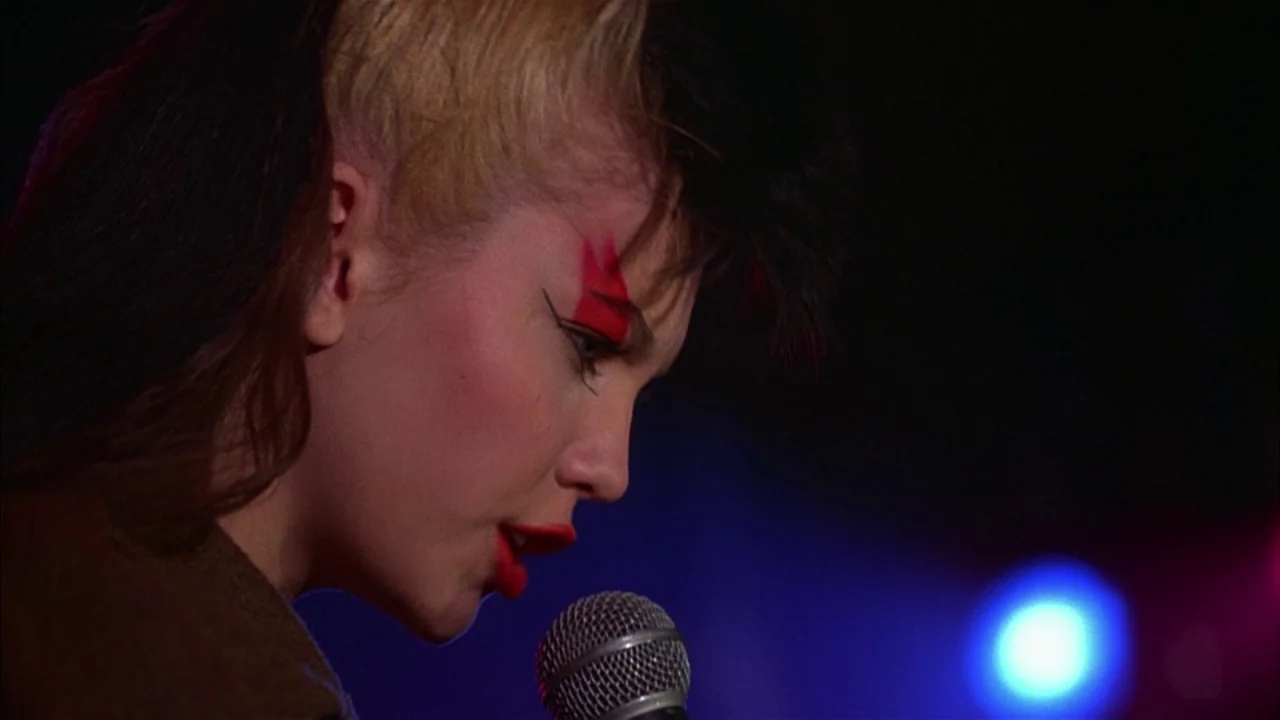 Ladies and Gentlemen, the Fabulous Stains (1985) movie still: closeup — A dimly lit performance area with dark shadows framing the subject. A woman…
