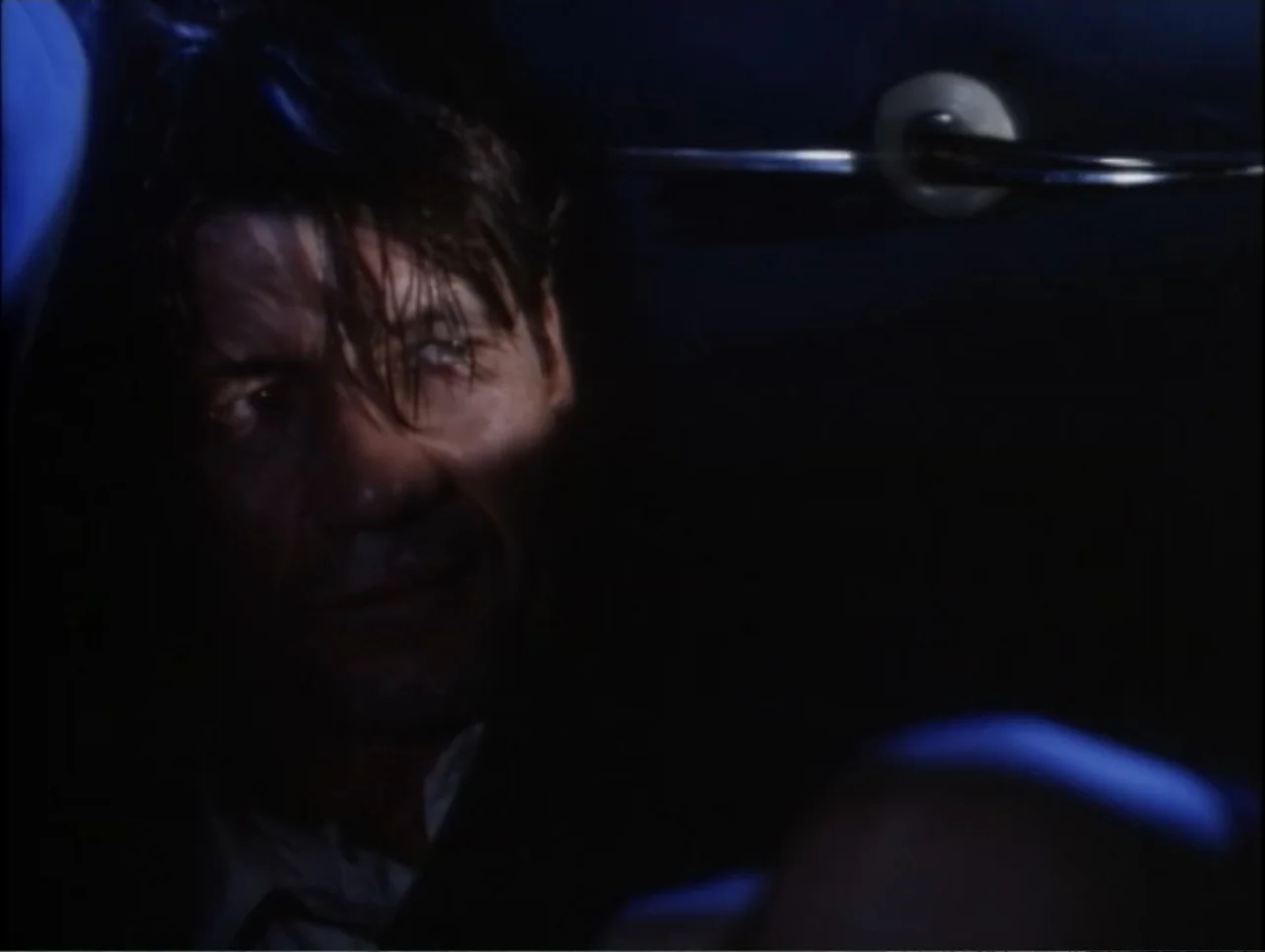 Cast a Deadly Spell (1991) movie still: closeup — A dark car interior at night with a single light reflecting off surfaces. A man sits in the driver…