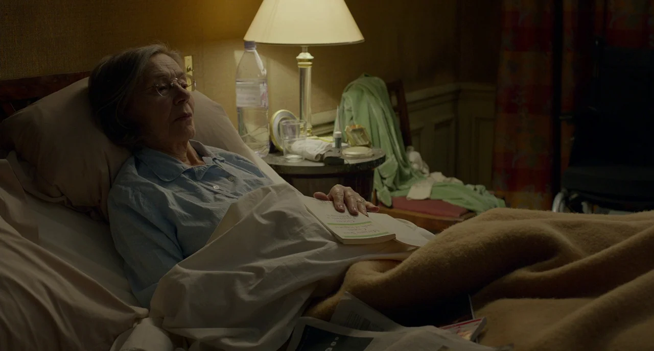 Amour (2012) movie still: medium — An elderly woman reclines in a dimly lit bedroom at night. She rests peacefully in bed with a book lying open on…