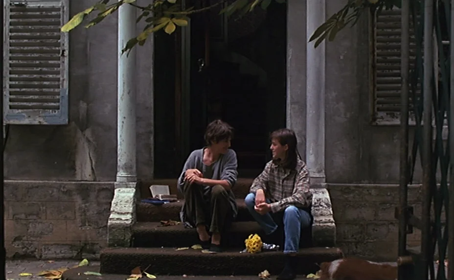 Kung Fu Master! (1988) movie still: fullbody — Two women sit on the front steps of a gray building with shuttered windows. The two subjects face…