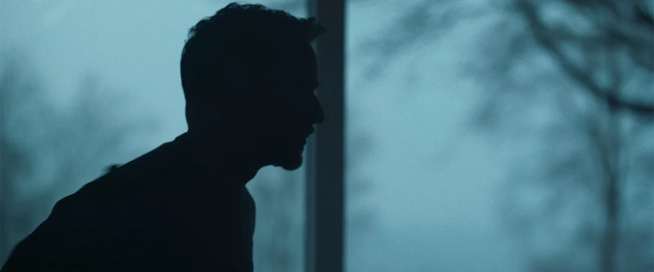 My Son (2021) movie still: closeup — A man is silhouetted against a bright, hazy window in a dim indoor space. The figure stands in profile looking…