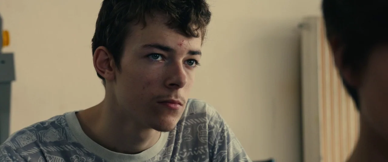 BPM (Beats Per Minute) (2017) movie still: closeup — A light-colored classroom wall features a radiator in the background. A young man listens…