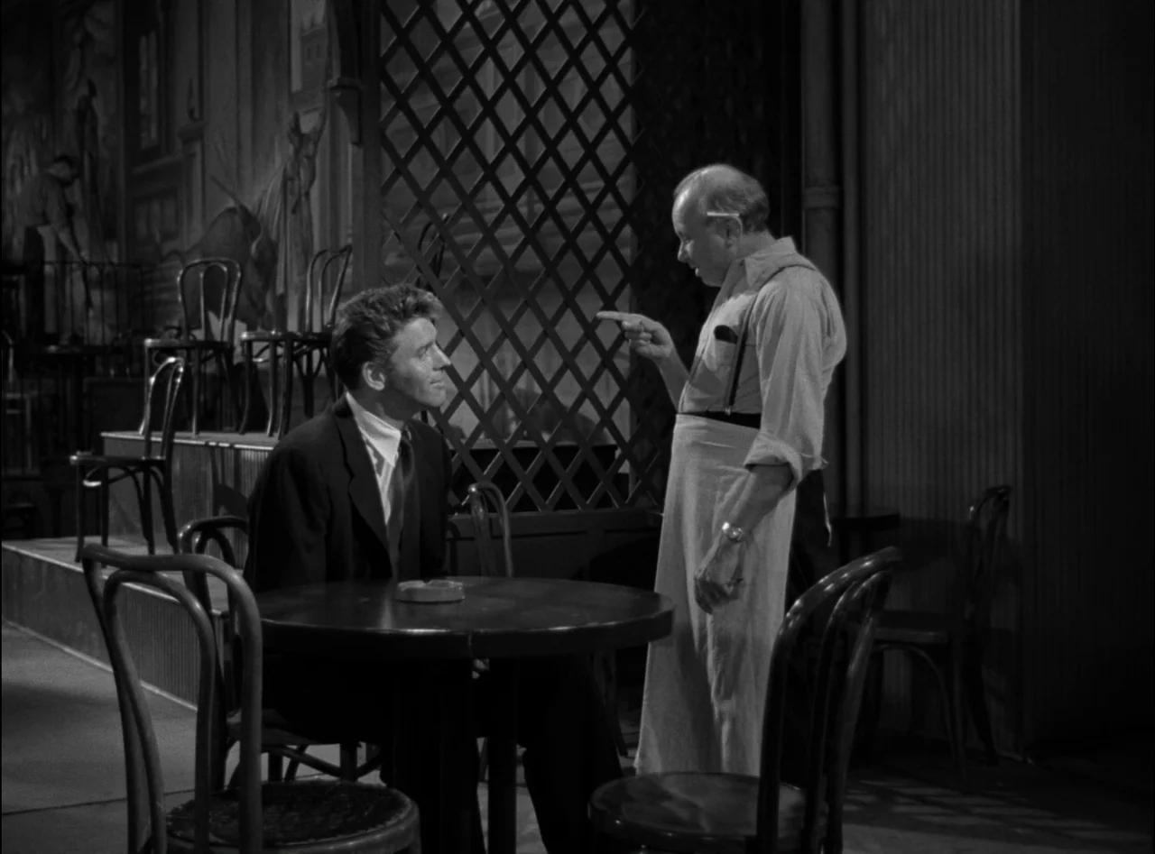 Criss Cross (1949) movie still: medium — A dark cafe interior features wooden chairs and a table with a lattice partition. An older waiter in an…