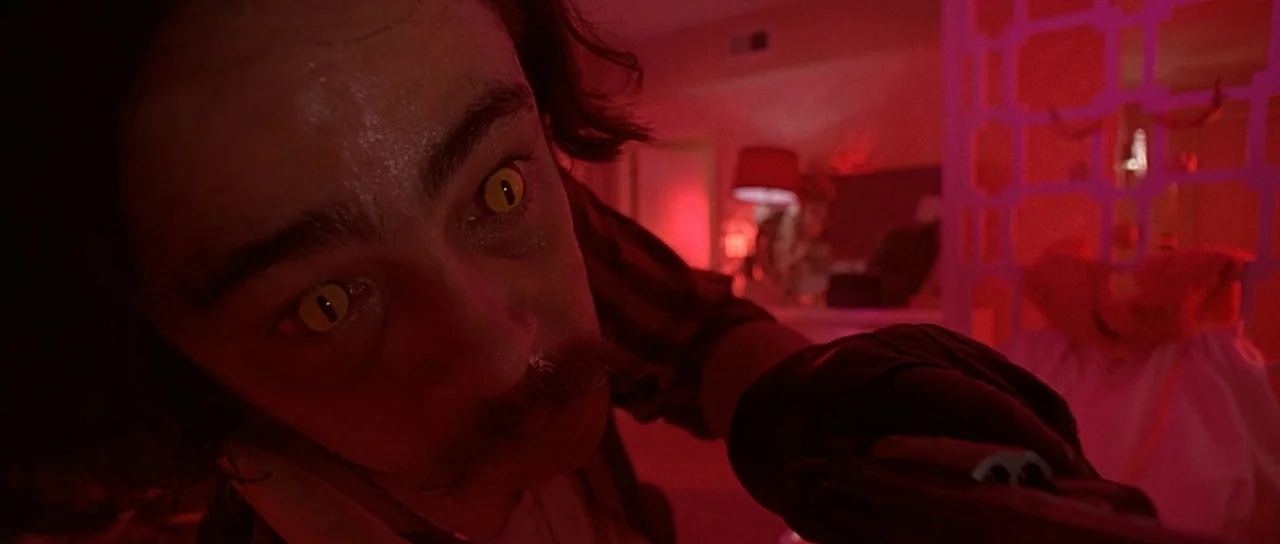 Fear and Loathing In Las Vegas (1998) movie still: closeup — A dark, dimly lit room is bathed in intense red light. A man with distinct cat-like…