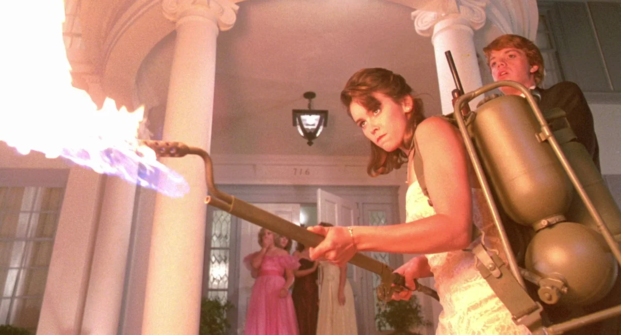 Night of the Creeps (1986) movie still: medium — A house entrance with white columns and steps at night with people in background. A woman in a…