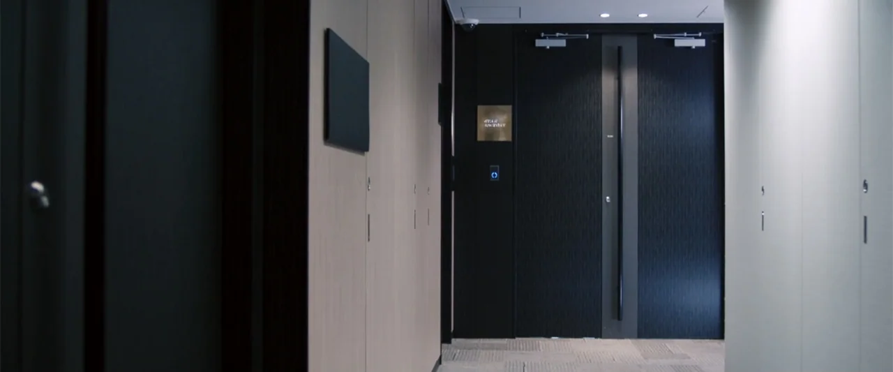 To Hear the Birds Singing (1995) movie still: medium — A modern office corridor features smooth light-colored wood wall panels and a dark textured…