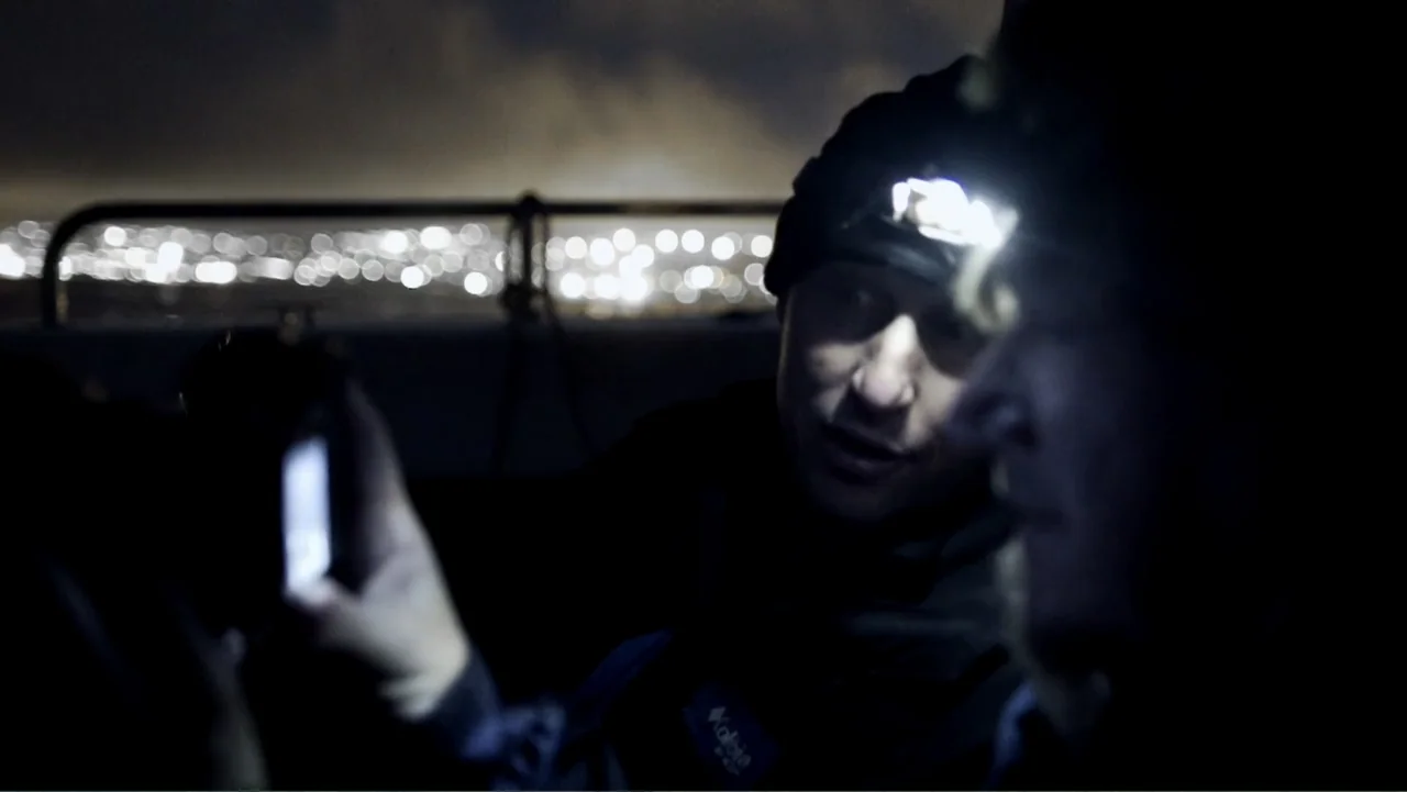 Air Jaws: Night Stalker (2016) movie still: medium — Two individuals stand on a dark outdoor deck at night with distant city lights blurred. One man…