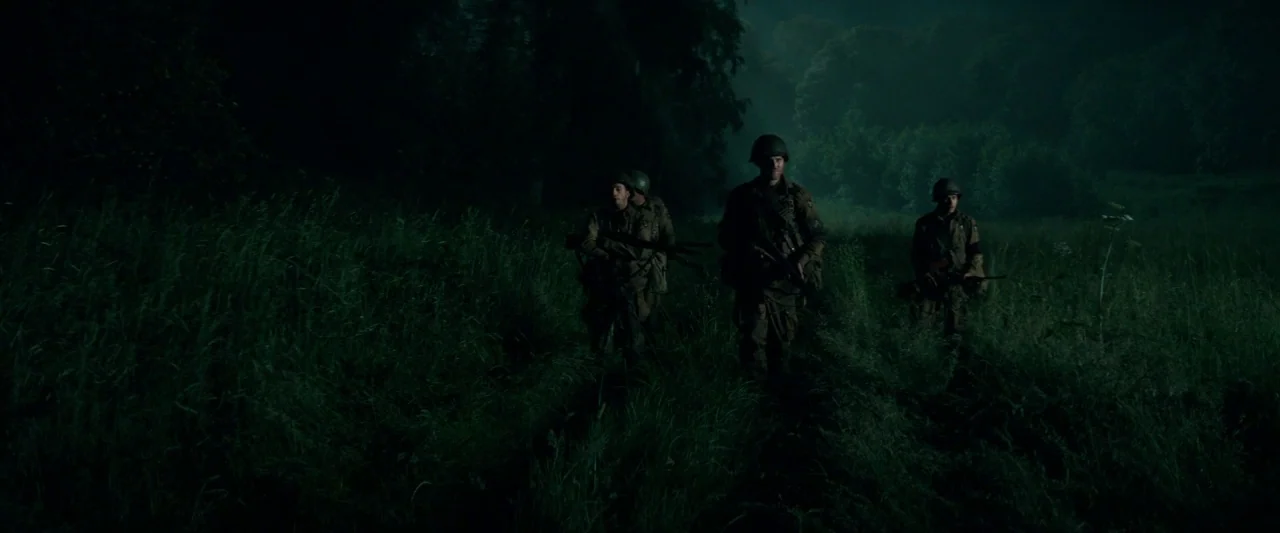 Overlord (2018) movie still: wide — A group of soldiers moves across a dark, overgrown meadow at night. The surrounding terrain is densely packed…