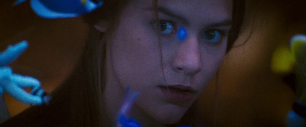 Romeo + Juliet (1996) movie still: closeup — A close view of a young woman appearing behind the glass of an aquarium. Several colorful fish swim in…