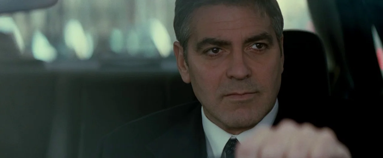 Michael Clayton (2007) movie still: closeup — The interior of a moving vehicle with a man focused on the road ahead. Sunlight enters through the…