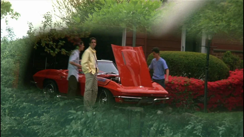 Goodfellas (1990) movie still: wide — Three men stand around a bright red convertible car parked in a residential driveway. Lush green bushes and…