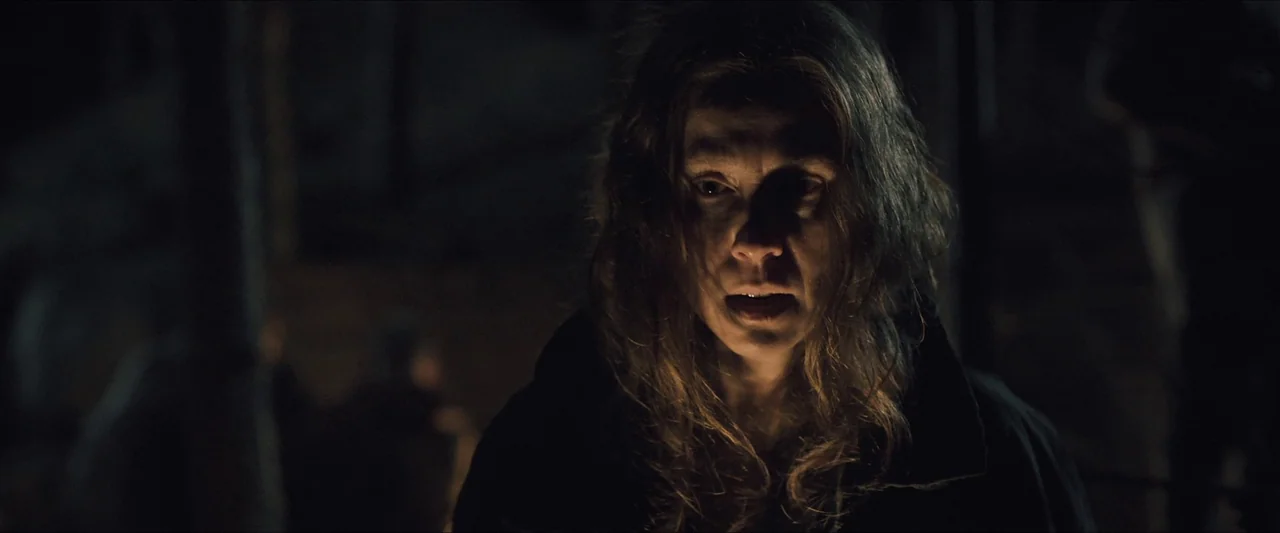 Azrael (2024) movie still: closeup — A dark outdoor space at night with indistinct trees in the background. A woman with long hair stands…