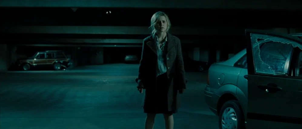Drag Me to Hell (2009) movie still: fullbody — A dimly lit multi-level parking garage featuring low concrete ceilings and parked vehicles. A young…