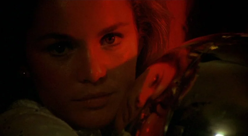 A Safe Place (1971) movie still: closeup — A dimly lit room is filled with intense red light. A young woman rests her face on her hand while looking…