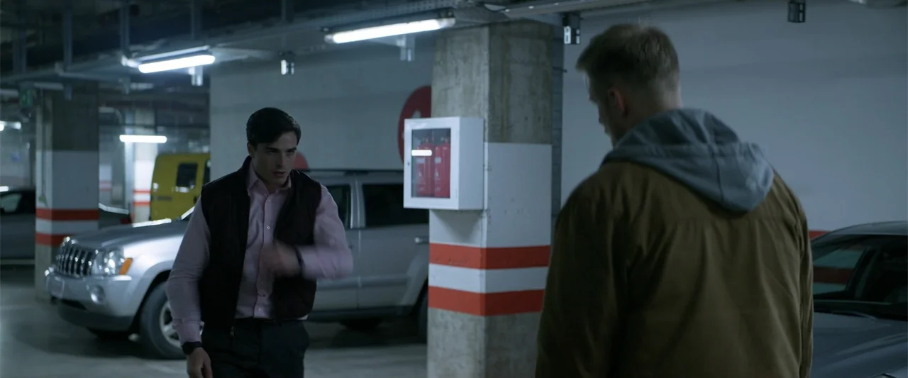 Marked Men: Rule + Shaw (2025) movie still: medium — An underground parking garage with concrete pillars and a white-painted wall with red stripes.…
