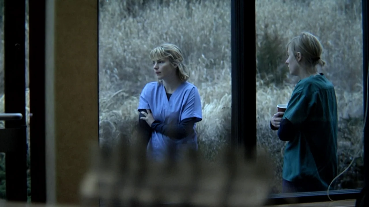 A Horrible Way To Die (2010) movie still: medium — Two women stand by a window overlooking a field of dead, dry grasses. The women are dressed in…