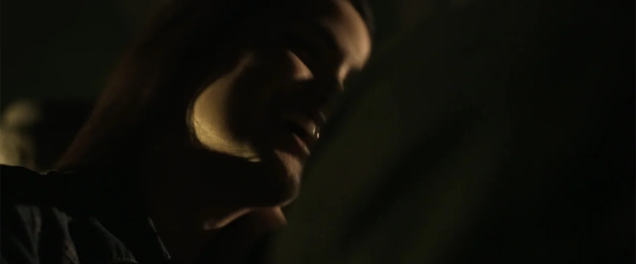 Kimura (2017) movie still: closeup — A dimly lit interior space is obscured by heavy shadows. A person's face is partially lit from the side as they…