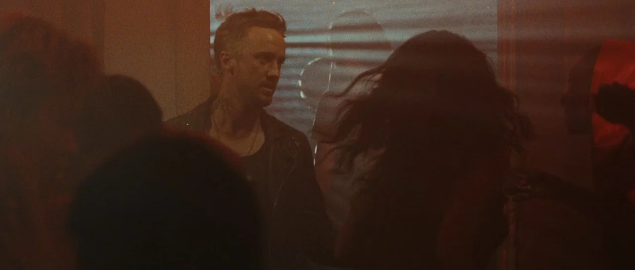 Message From The King (2016) movie still: medium — A dimly lit club interior filled with red light and horizontal shadows from blinds. A man stands…